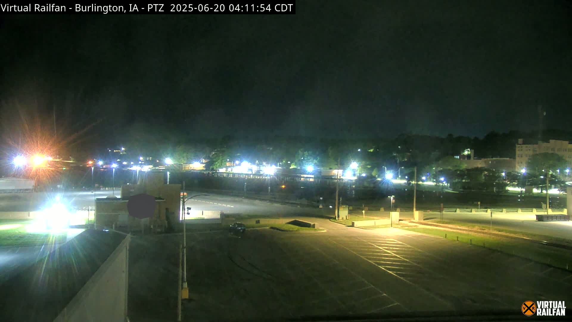 A nighttime view of a mostly empty parking lot and surrounding buildings under a clear, dark sky.
