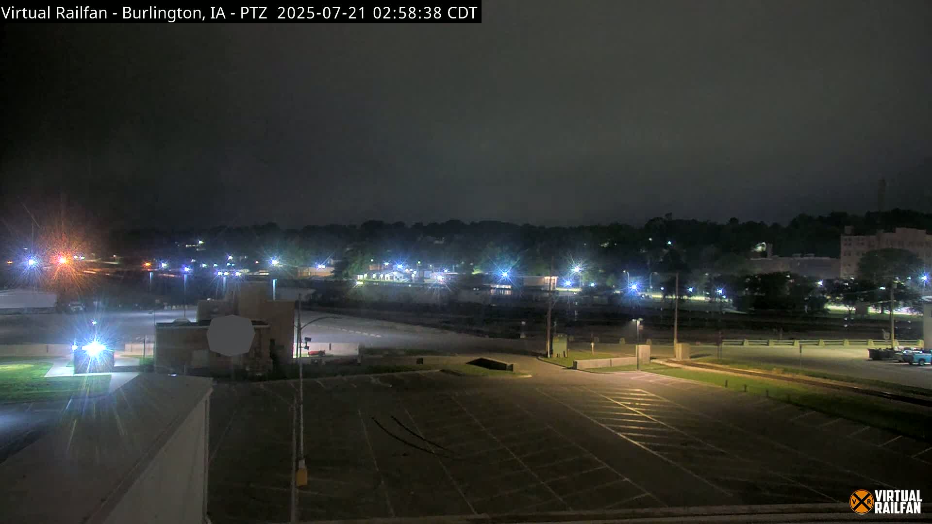 A nighttime view of an empty parking lot overlooking a dimly lit town under an overcast sky.