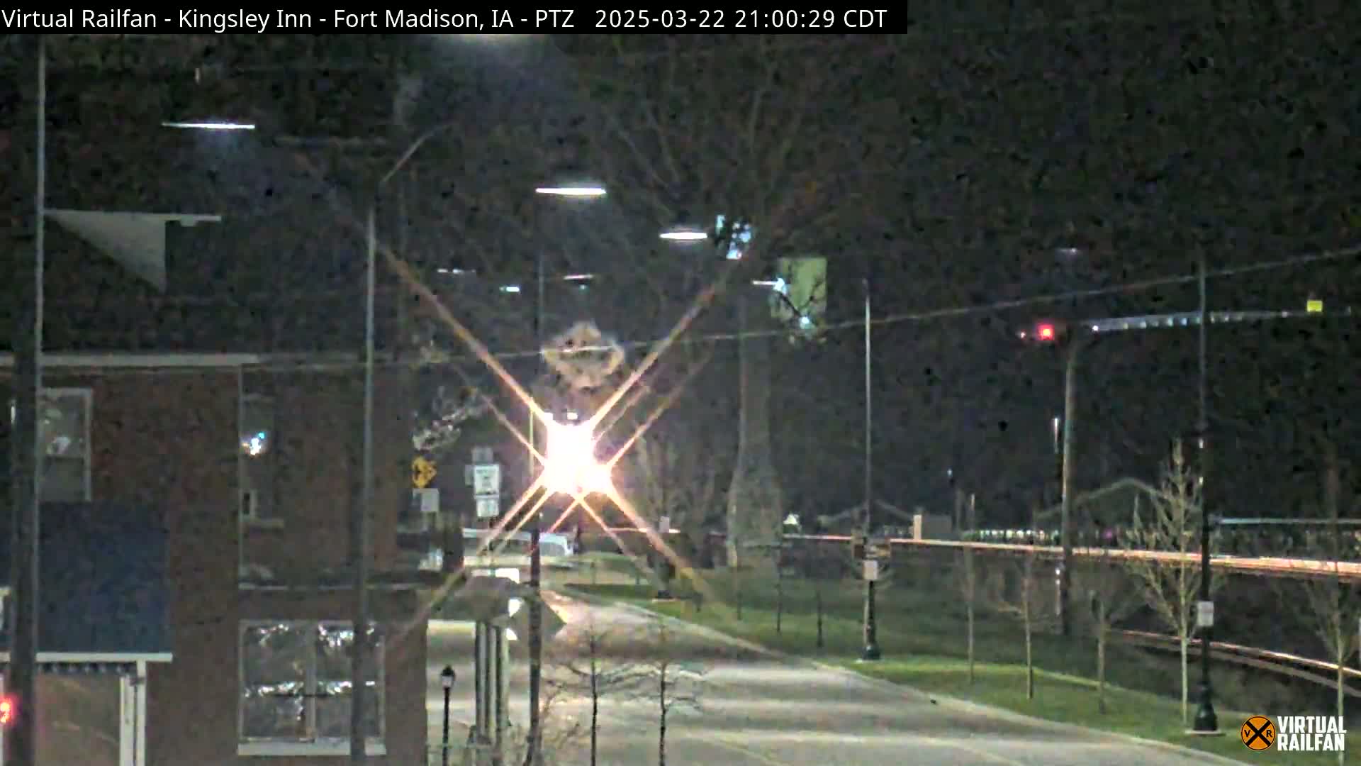 A nighttime street scene shows a brick building on the left, a roadway with streetlights, and trees along a bridge in the background.