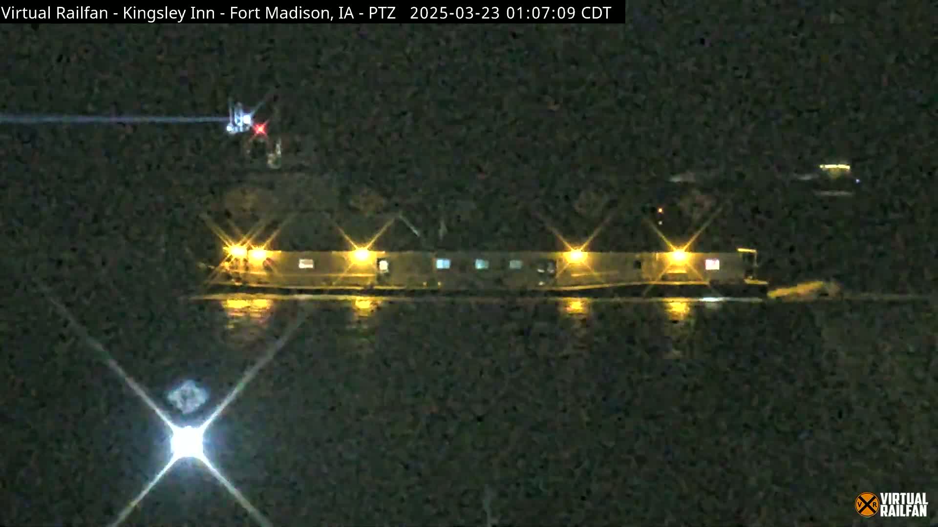 A long, low building with illuminated windows is reflected in dark water at night.