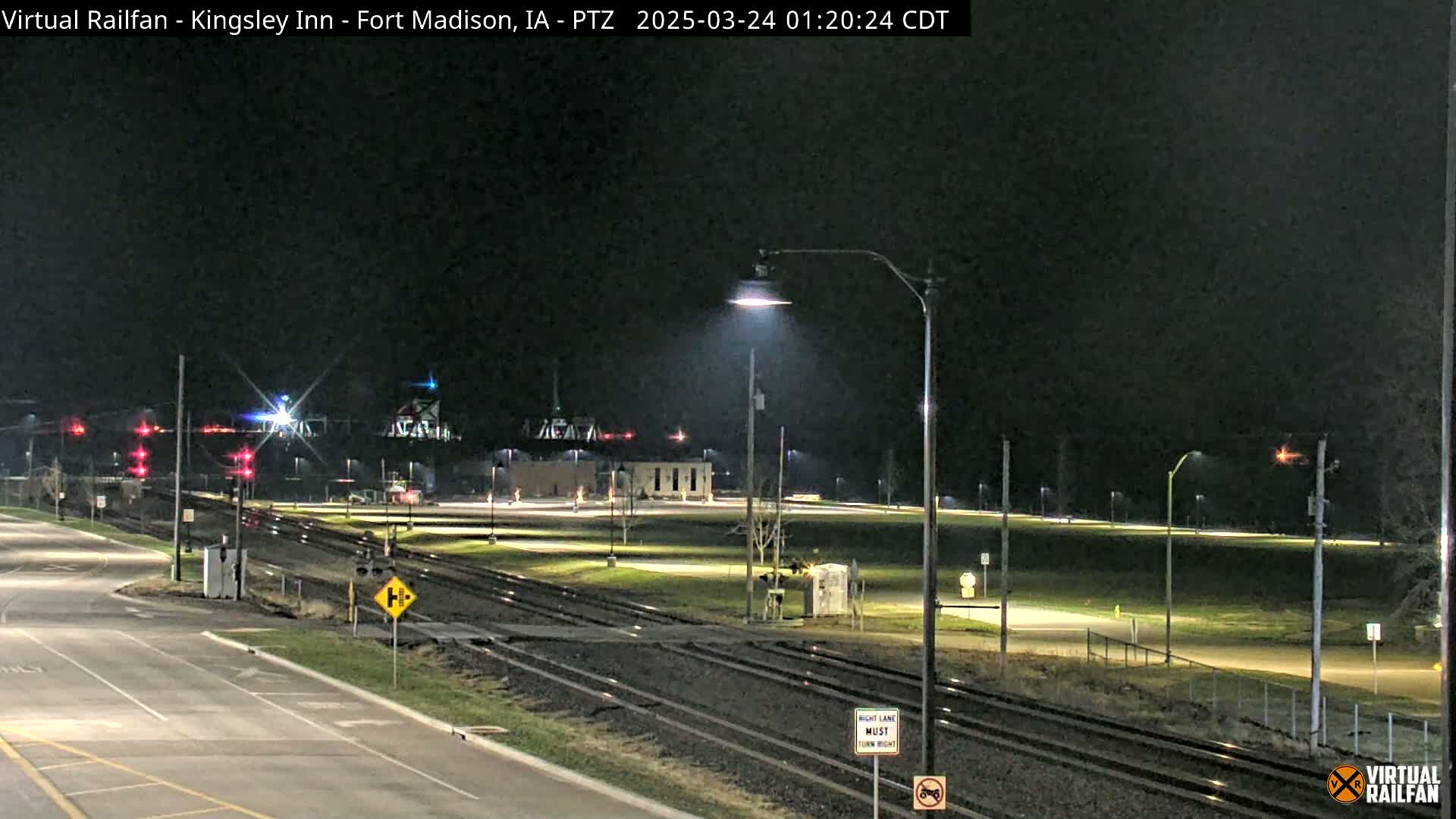 A nighttime view of a railroad crossing with a road and several streetlights, under clear skies.