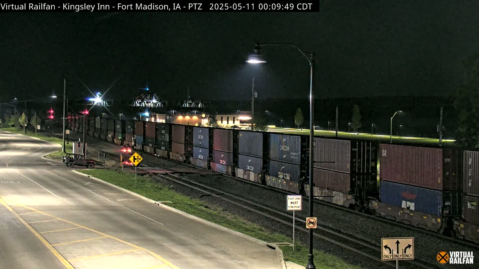 A long freight train carrying stacked shipping containers sits on railroad tracks at night next to a road.