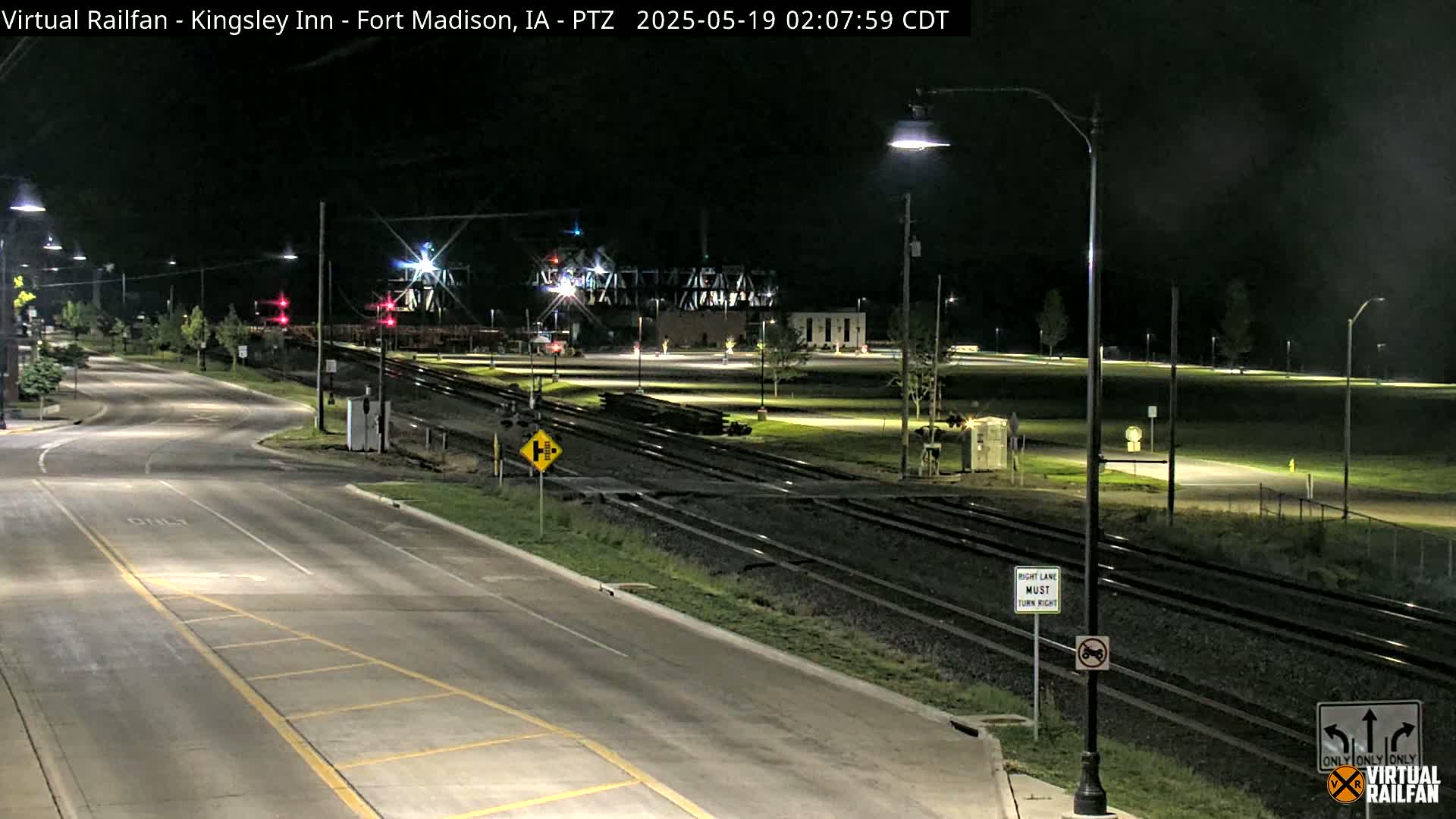 A nighttime view of a road intersecting railroad tracks, with several streetlights illuminating the scene.
