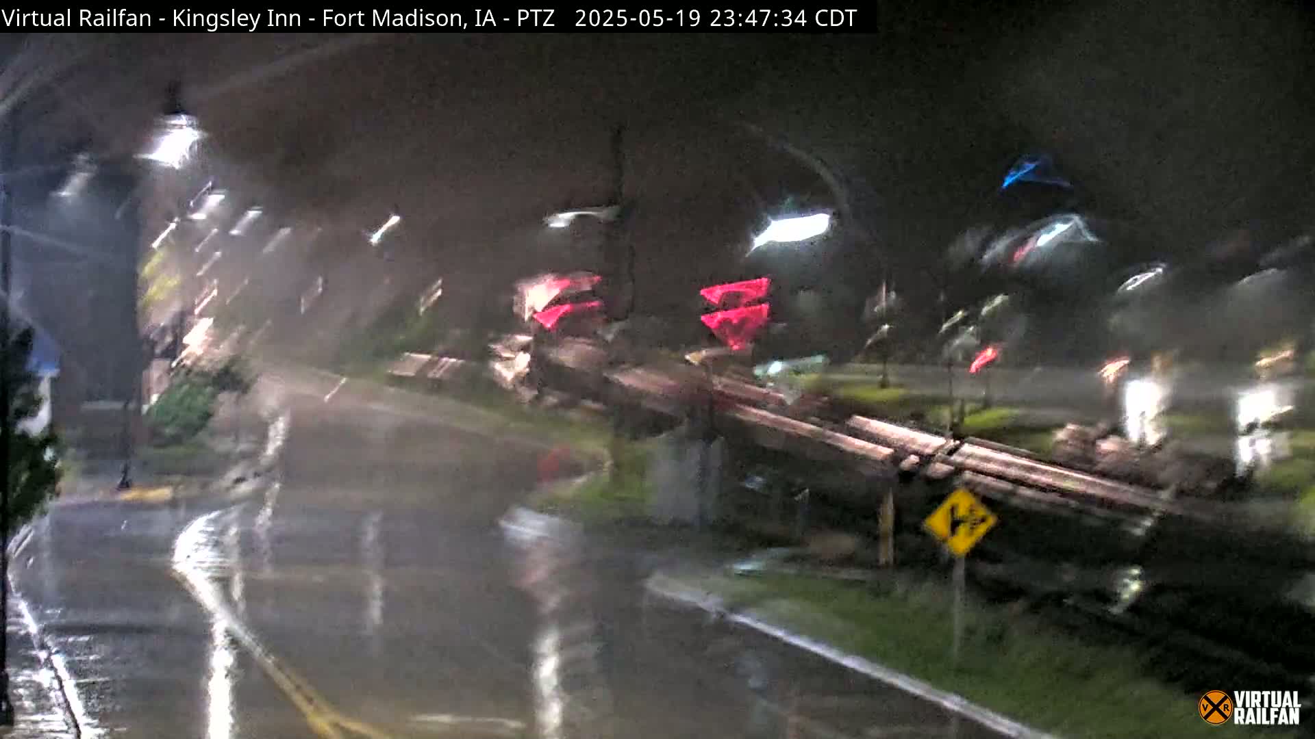 A nighttime view of a rain-soaked street intersection with blurred vehicles and streetlights under heavy rainfall.