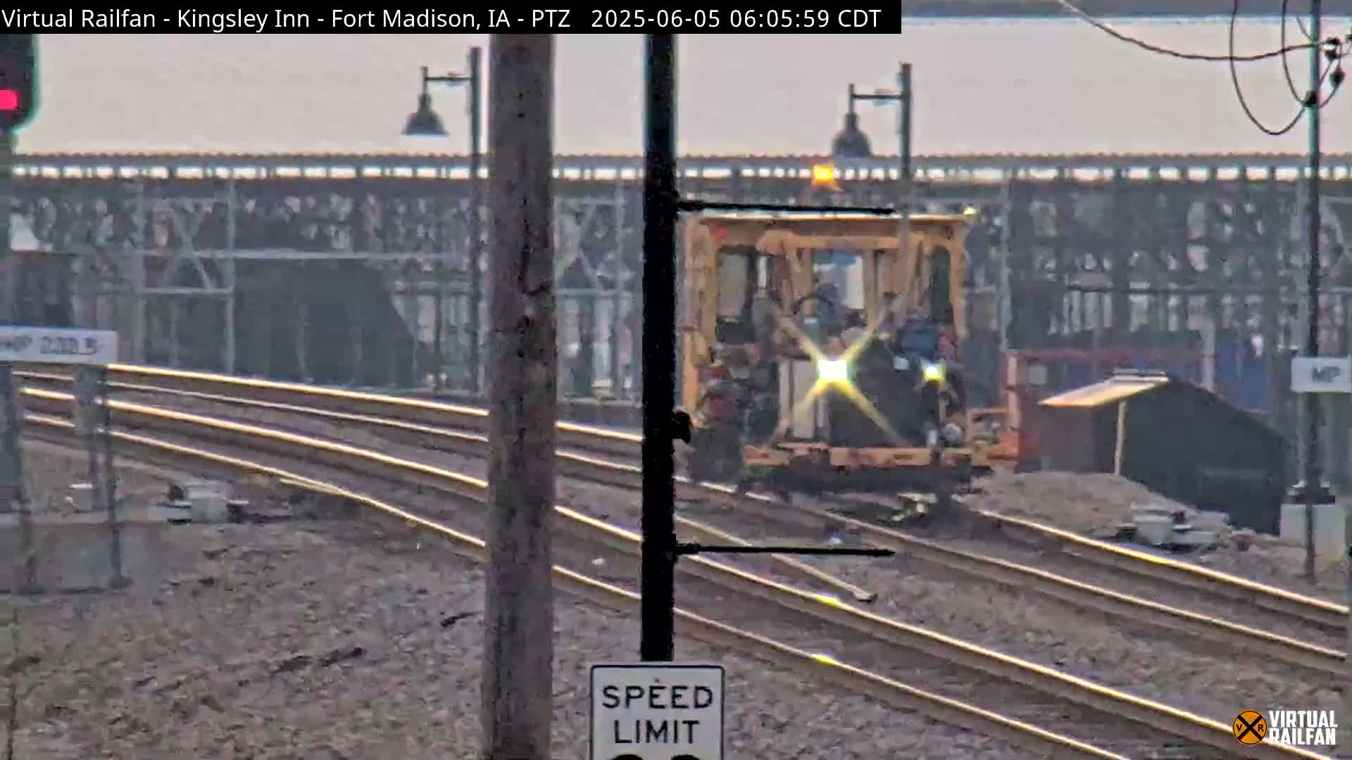 A yellow piece of railway maintenance equipment moves along a set of train tracks on a hazy day.
