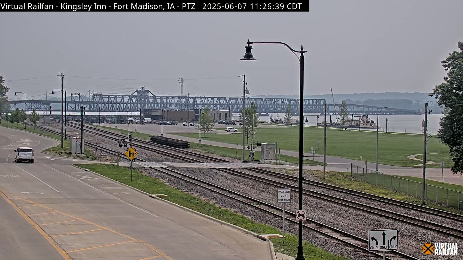 A view of train tracks and a road leading to a river with a large bridge in the background on a hazy day.