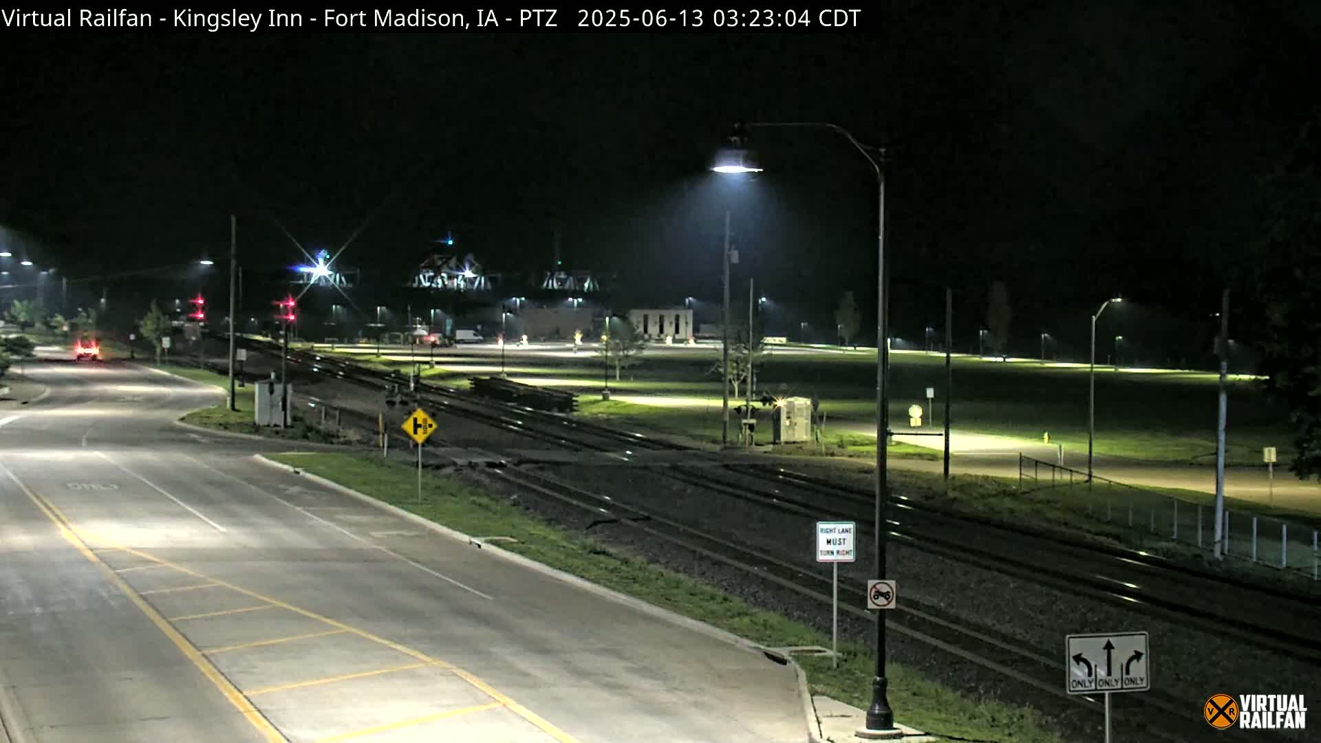 A nighttime view of a road intersecting with railroad tracks, under well-lit conditions.