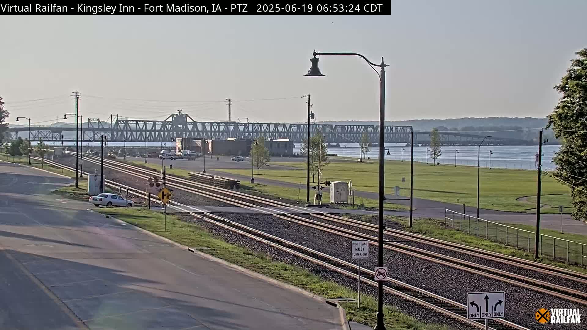 A view of a river, a bridge, railroad tracks, and a road on a partly sunny morning.