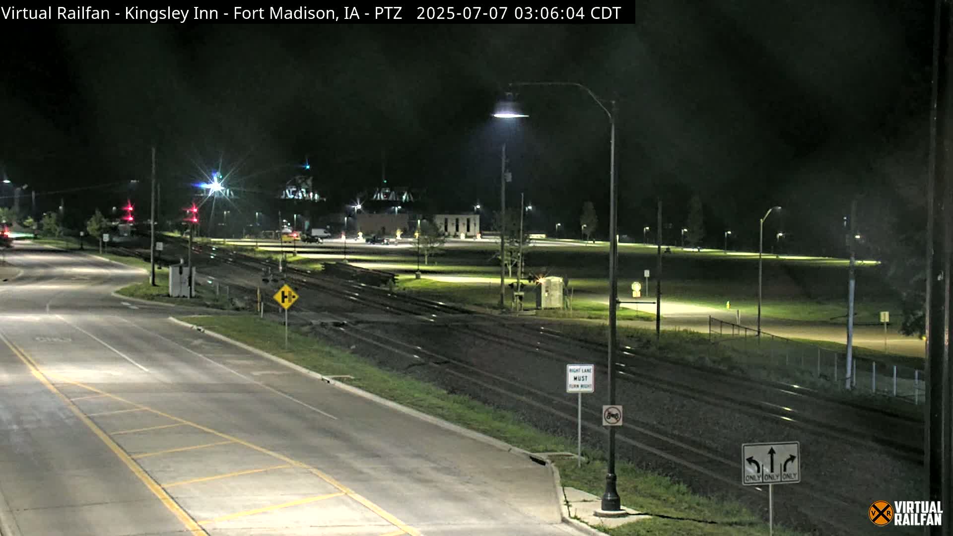 A nighttime view of a road intersection near railroad tracks, with streetlights illuminating the scene.