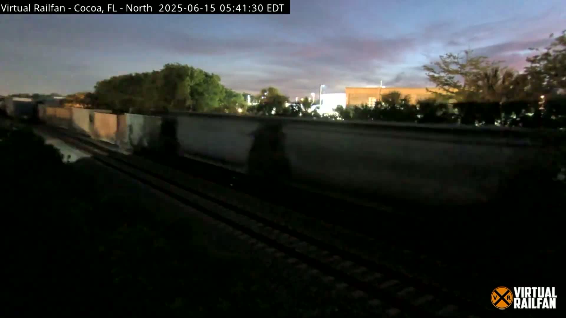 A long freight train passes by under a twilight sky.