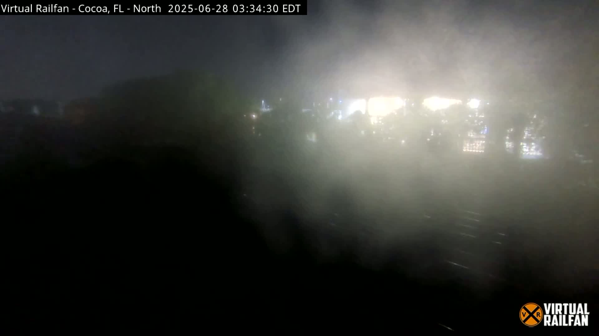 A nighttime view shows a hazy or foggy scene of what appears to be train tracks and distant lights.