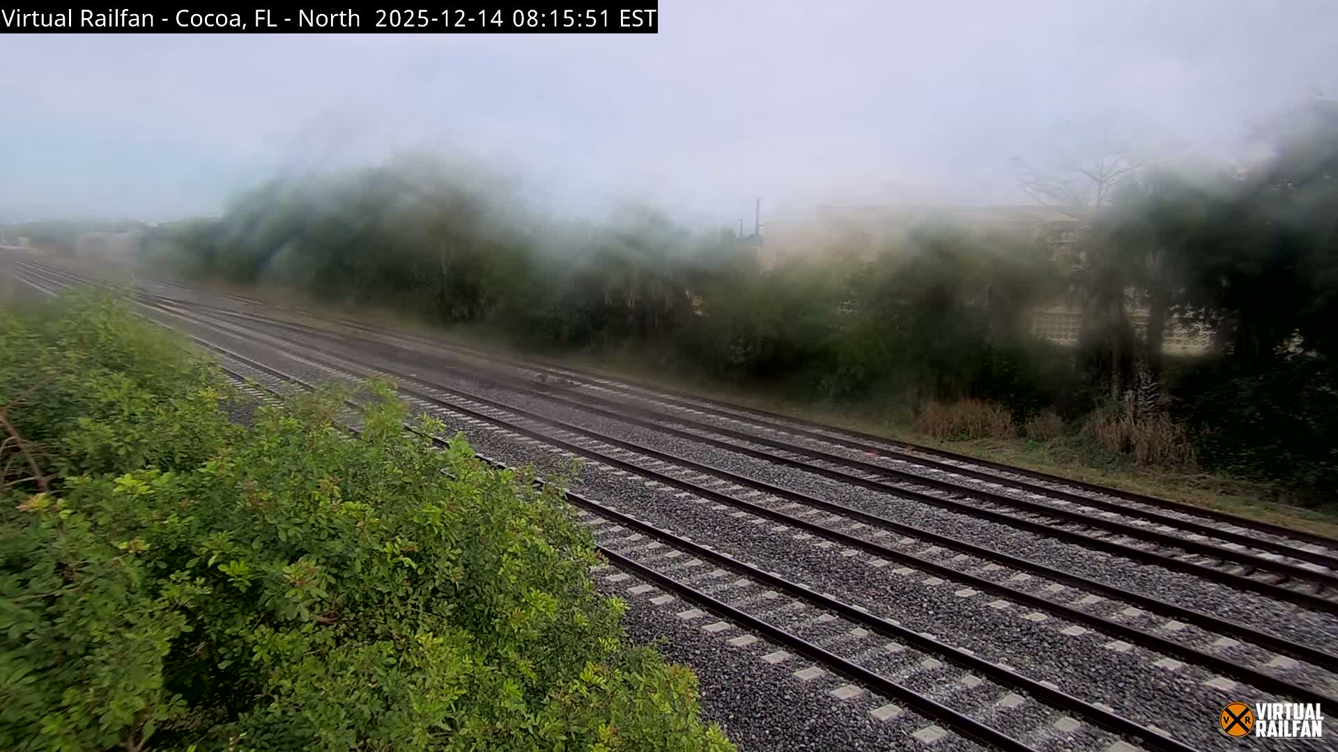 Dark train tracks curve into the foggy night, with diffused bright lights illuminating the dense mist in the background.