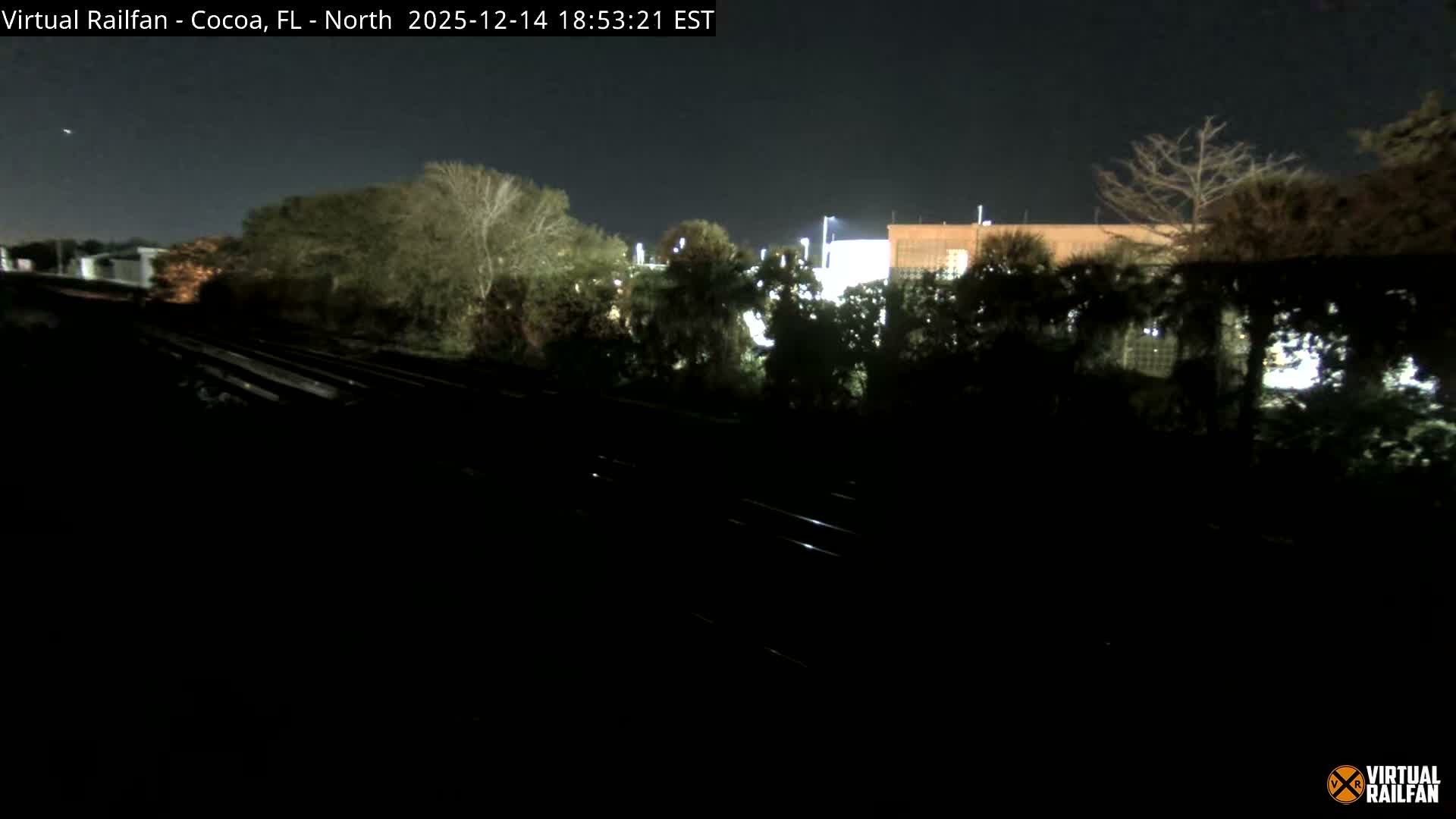 Dark train tracks curve into the foggy night, with diffused bright lights illuminating the dense mist in the background.