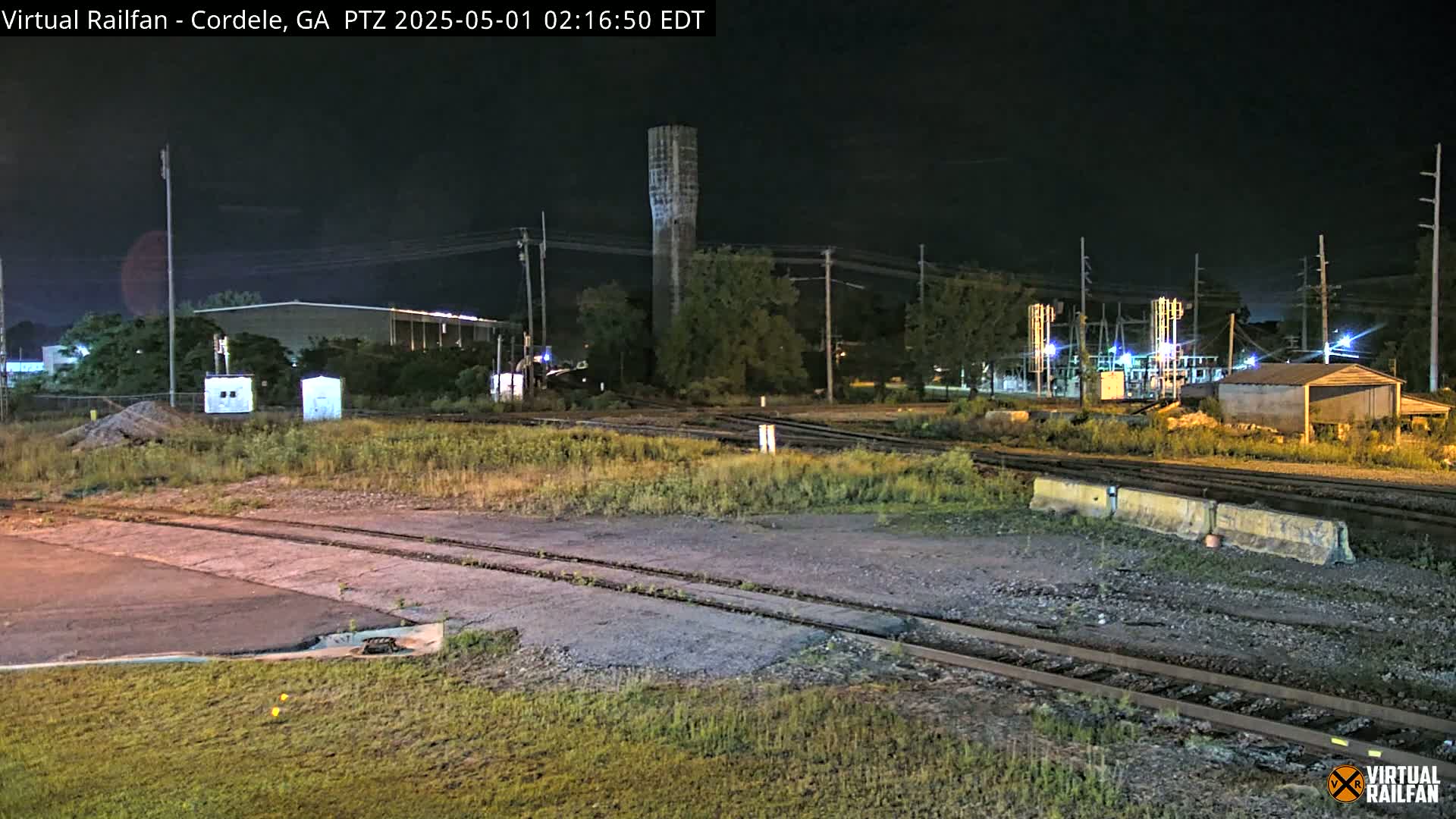 A nighttime view of a rail yard with a tall tower in the background, under clear skies.