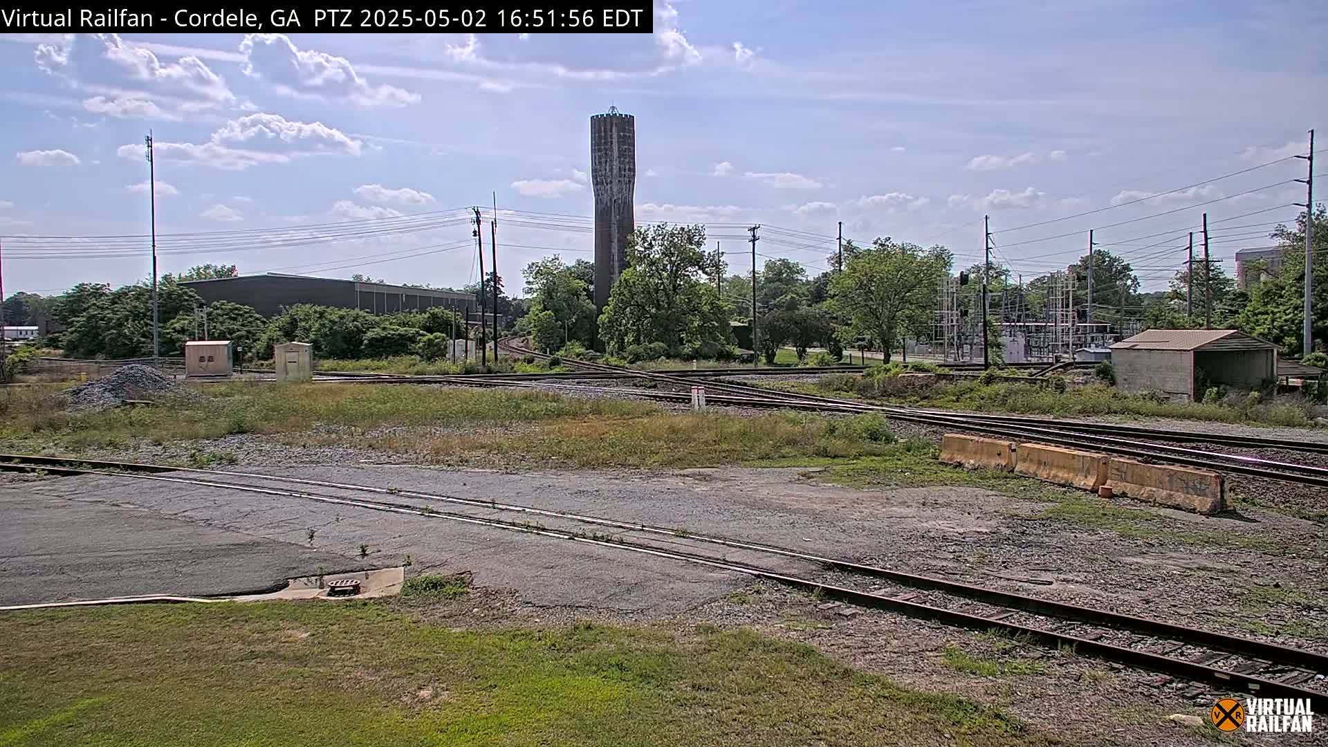 A view of a railway switching yard with a tall water tower in the background under a partly cloudy sky.