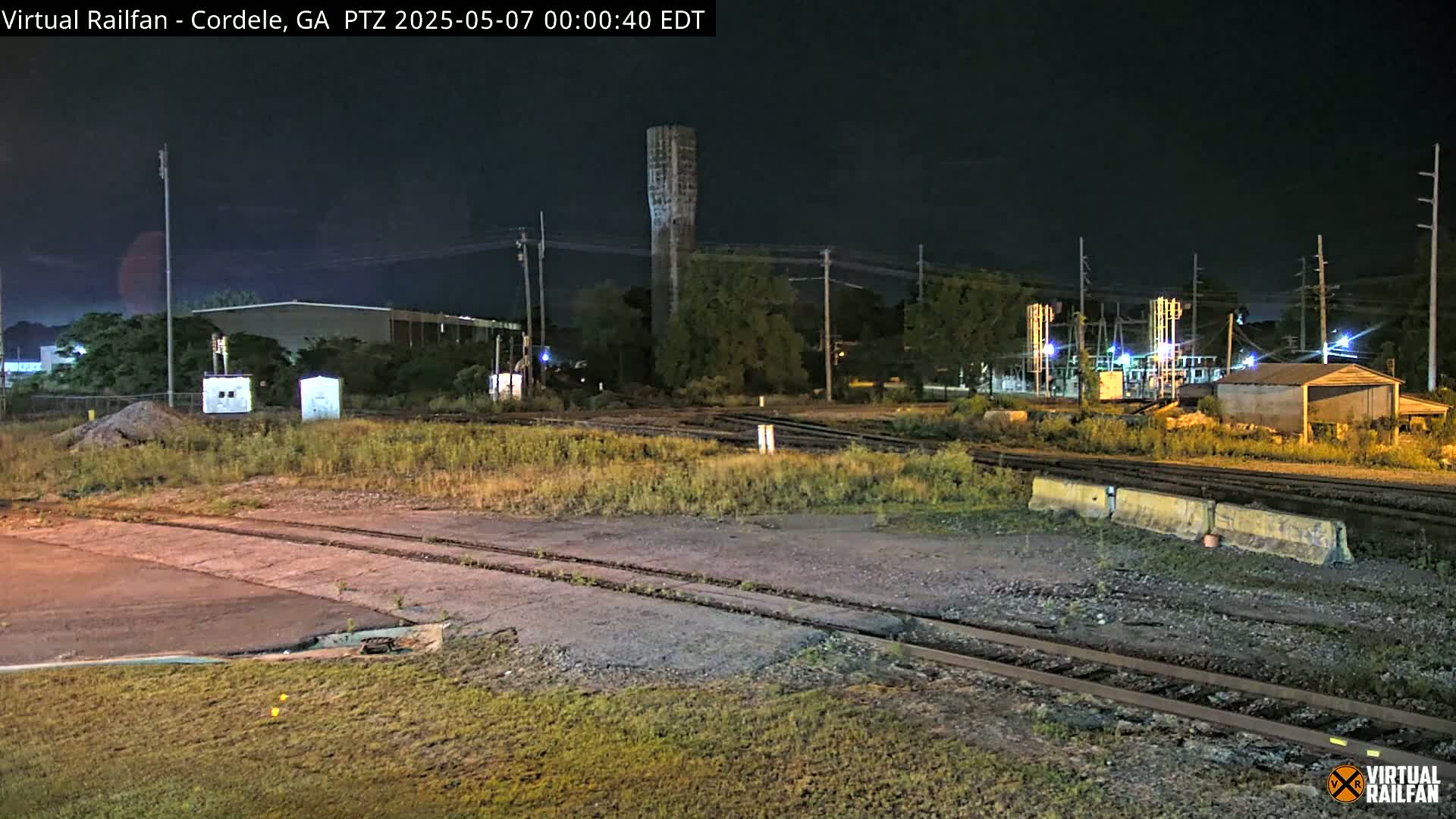 A nighttime view of a rail yard with a water tower in the background, under a clear, dark sky.