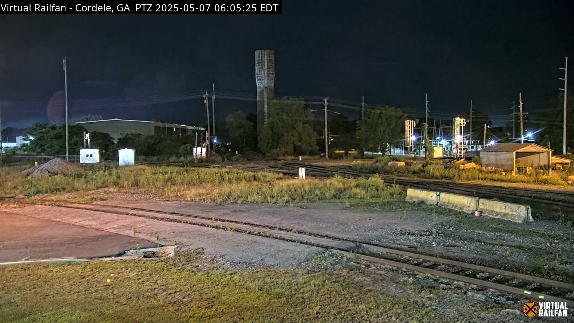 A nighttime view of a railroad yard with a water tower in the background under a dark sky.