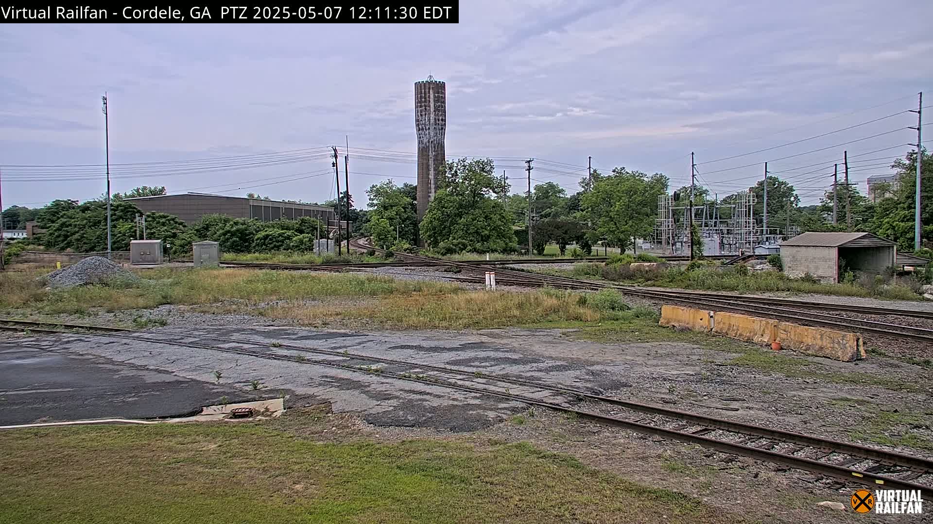 A railway switching yard with a tall water tower in the background under an overcast sky.
