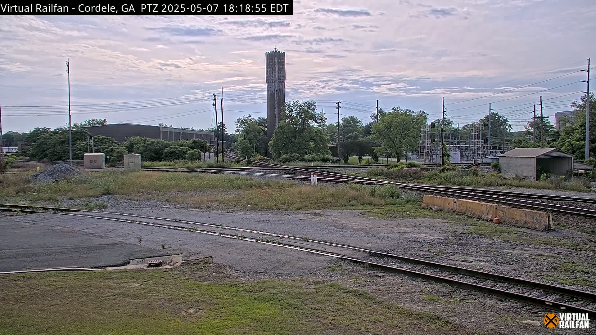 A railway switching yard with a tall water tower in the background under a partly cloudy sky.