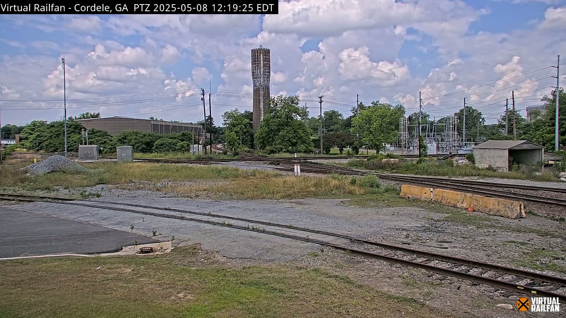 A view of a railroad switching yard under partly cloudy skies, with a water tower visible in the background.