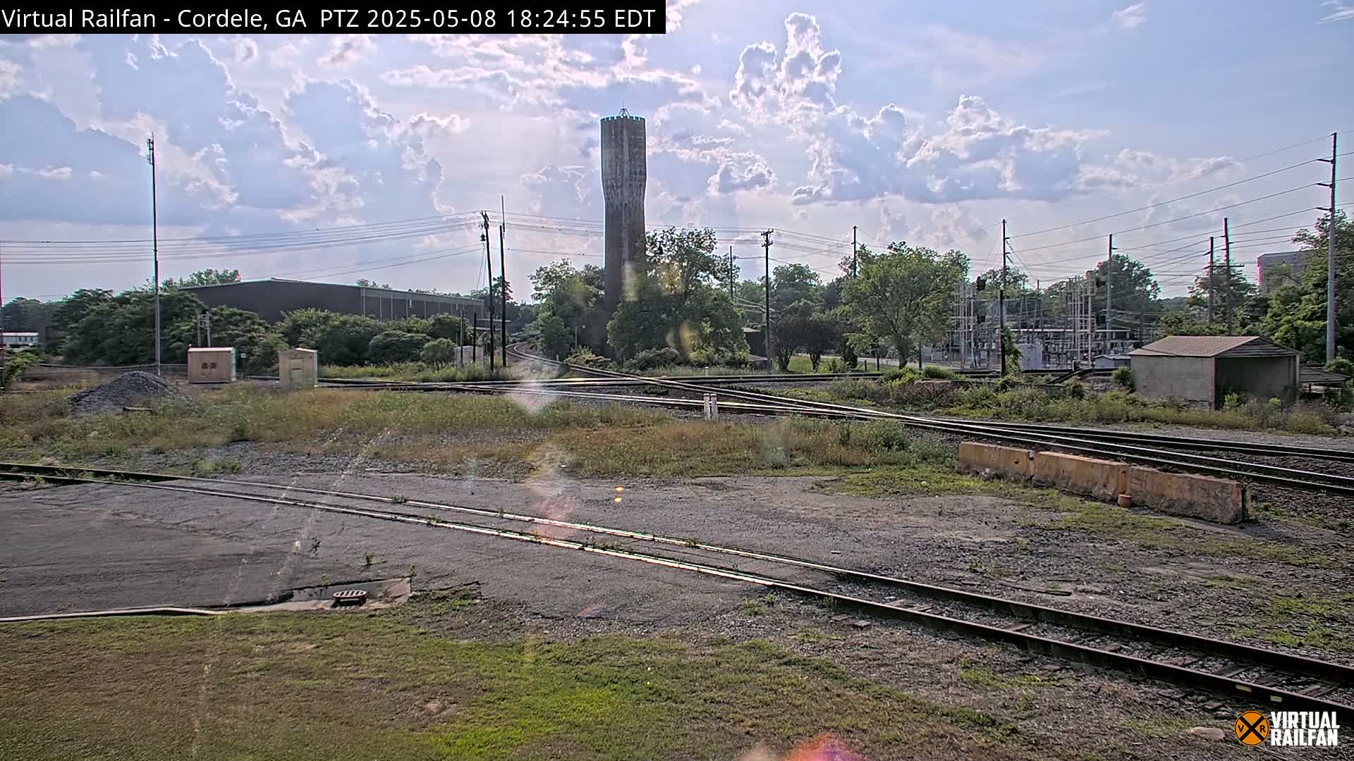 A partly cloudy sky overlooks a railroad switching yard with a tall water tower in the background.