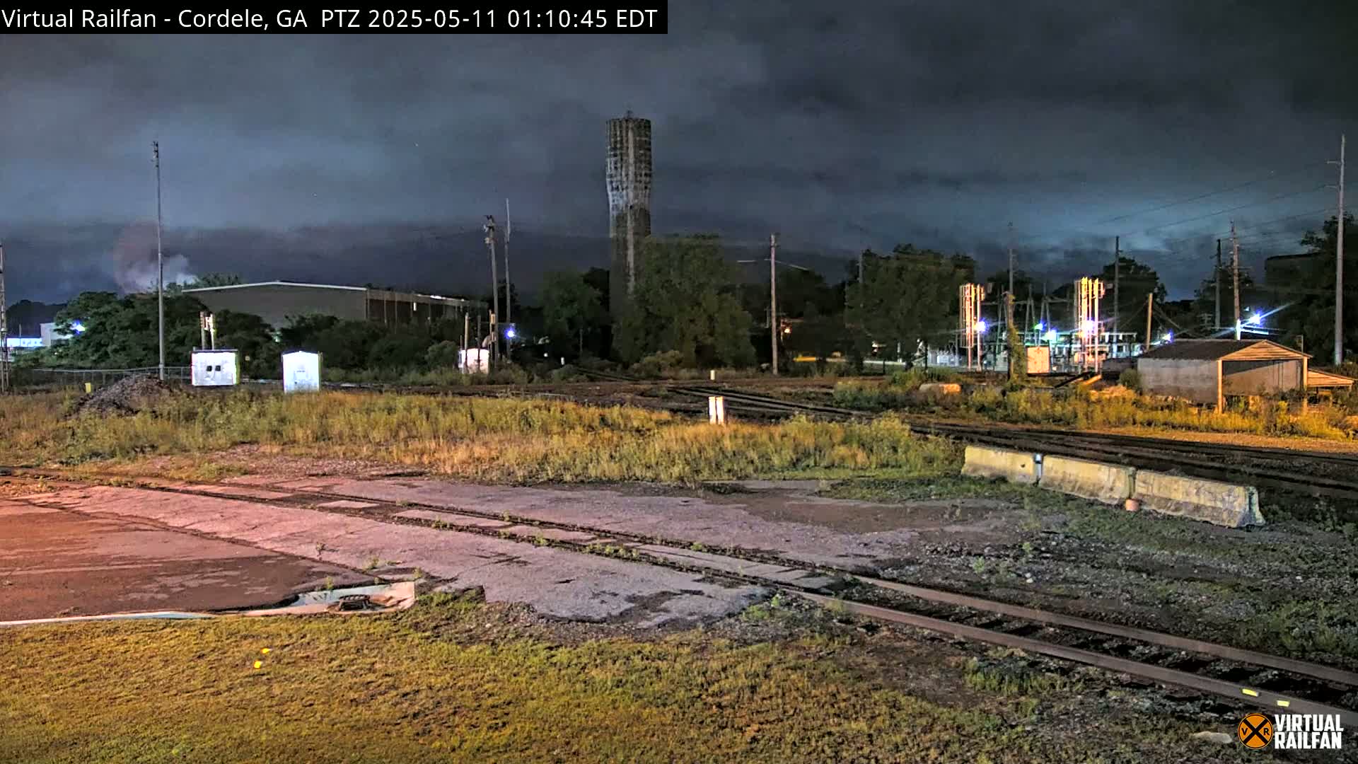 A nighttime view of railroad tracks and industrial buildings under a cloudy sky.