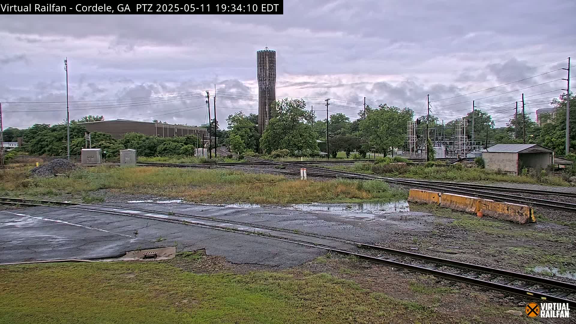A railroad crossing with a tall water tower in the background under an overcast sky.