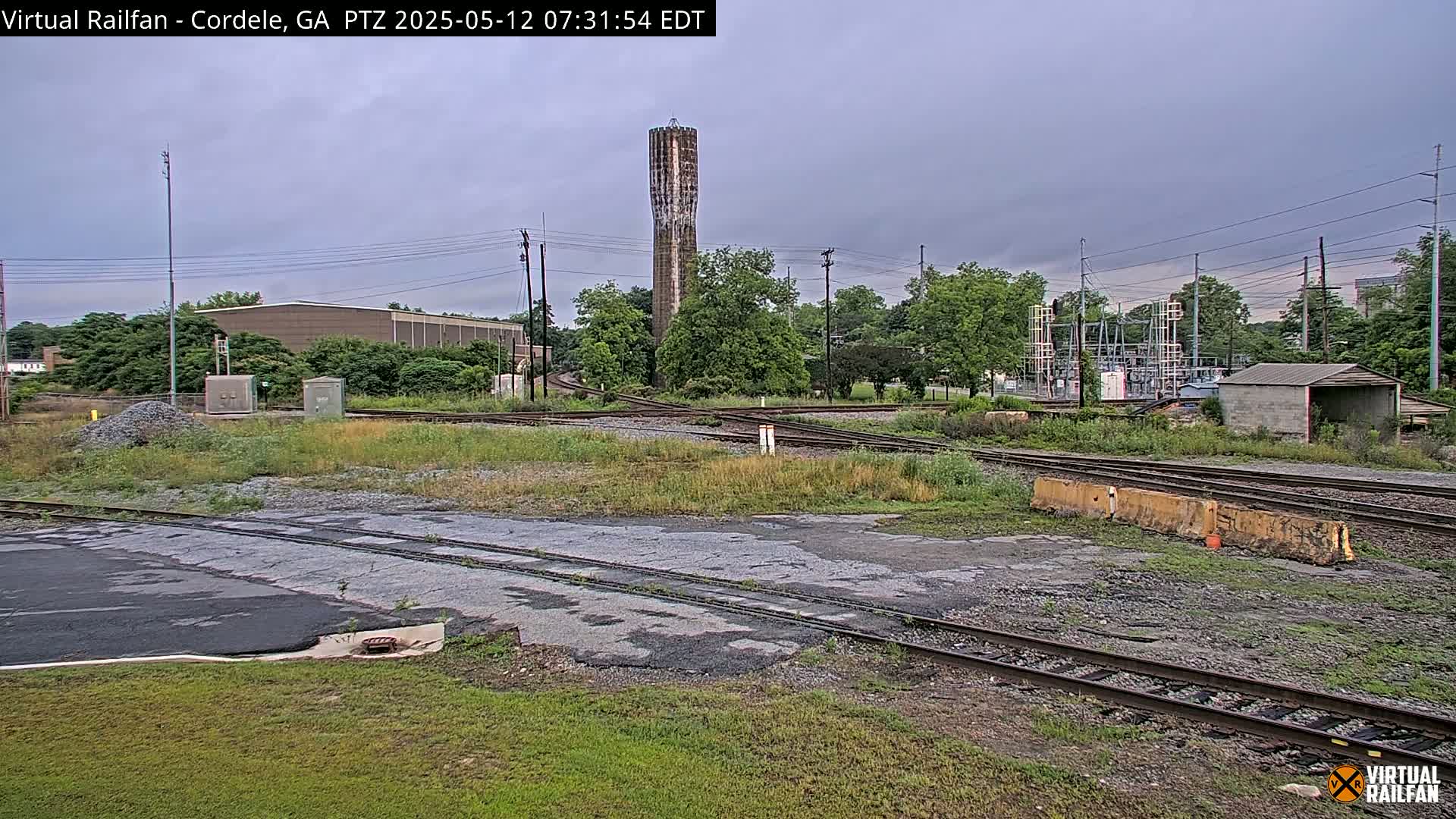 A view of a railway switching yard with a tall water tower in the background under an overcast sky.