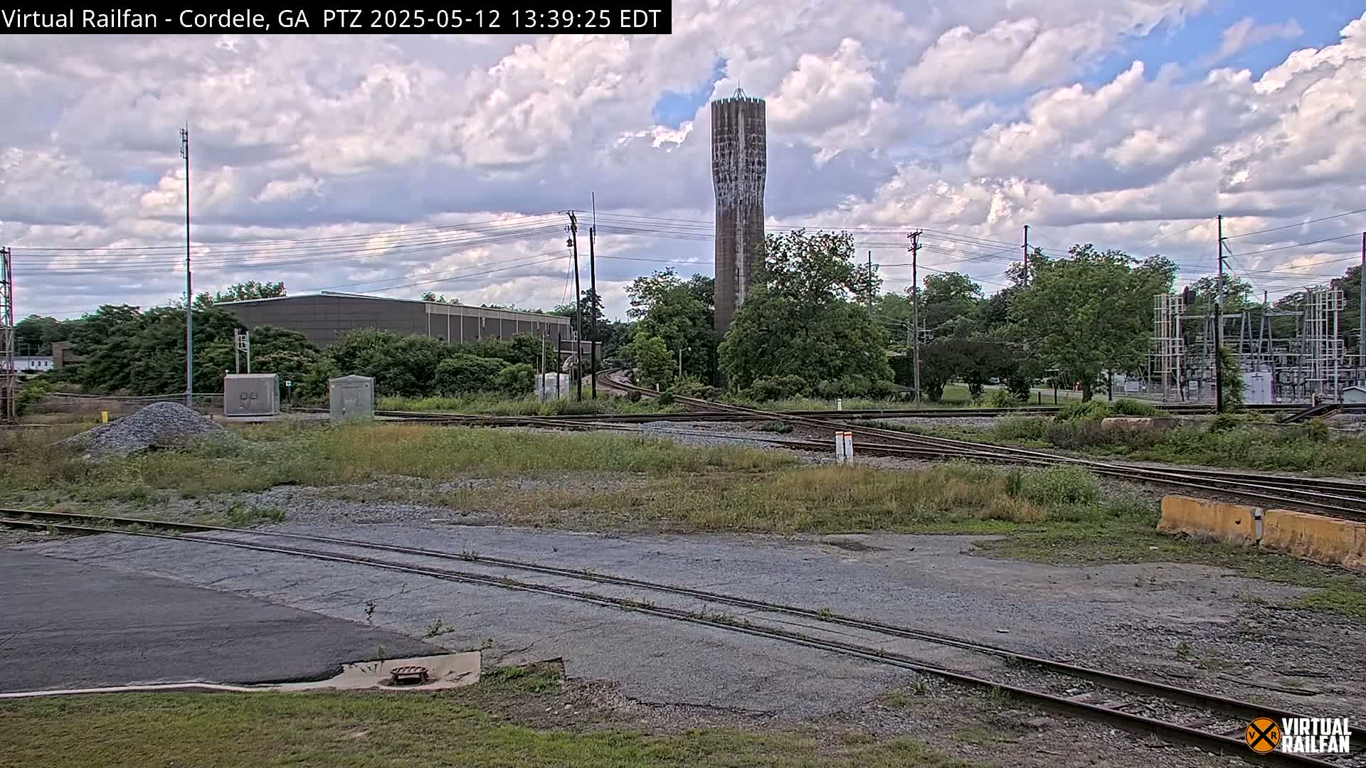 A partly cloudy sky overlooks a railroad switching yard with a tall water tower in the background.