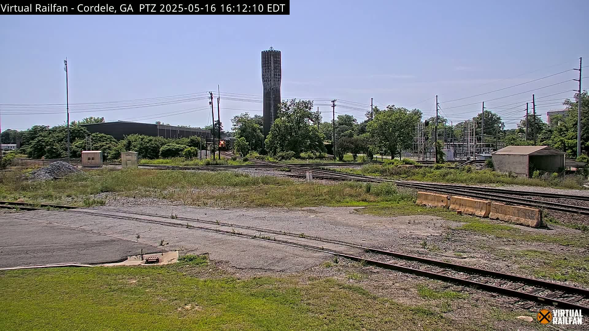 A train passes through a railroad yard on a sunny day, with a tall water tower visible in the background.