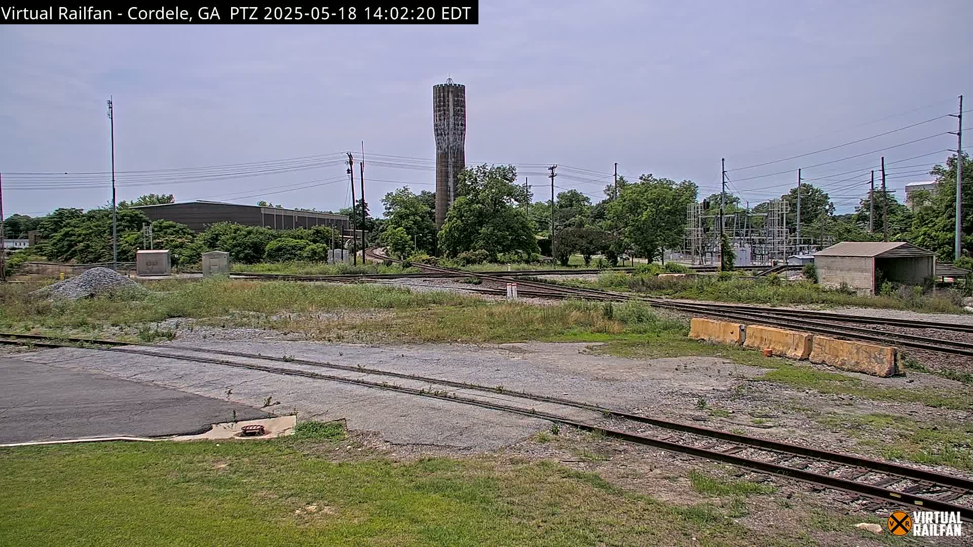 A view of a railway switching yard on a partly sunny day, with a tall water tower visible in the background.