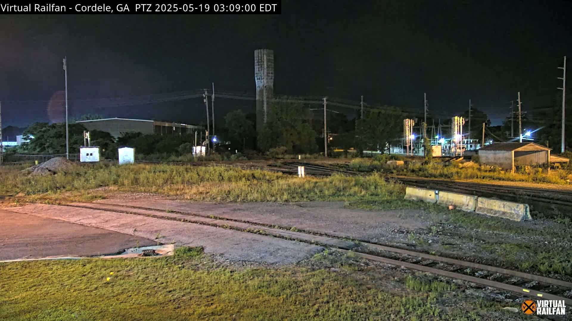 A nighttime view of a railway switching yard with a water tower in the background under a clear, dark sky.