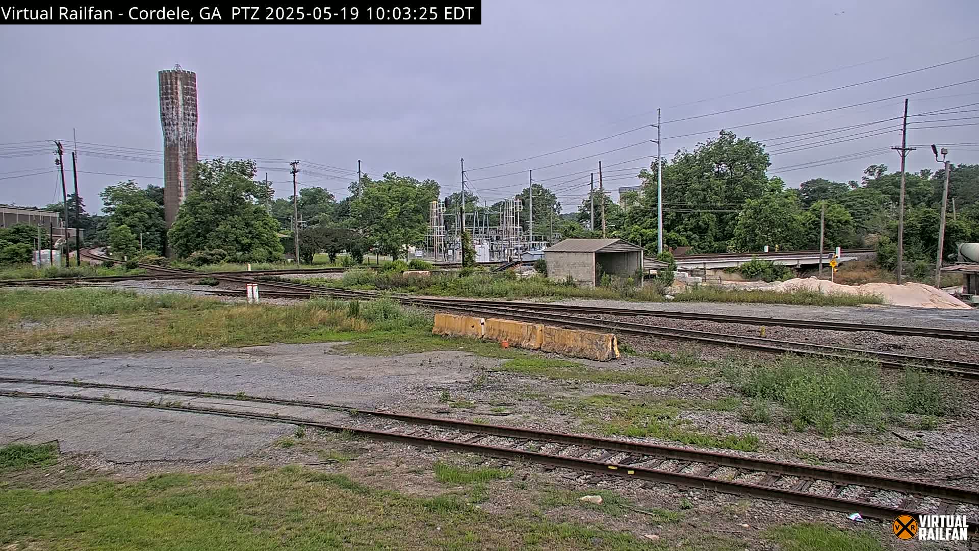 A railway switching yard with a tall water tower in the background under an overcast sky.