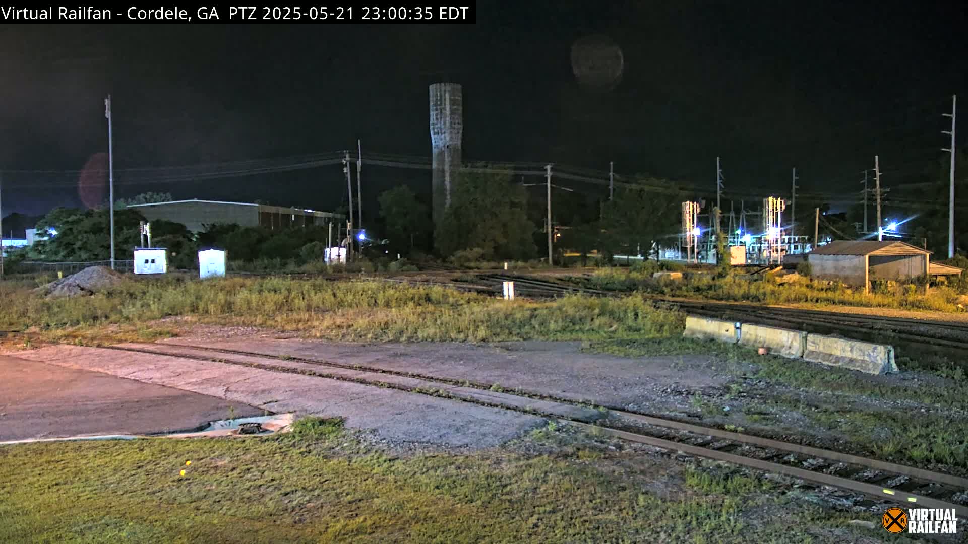 A nighttime view of a rail yard with a water tower in the background under a clear sky.