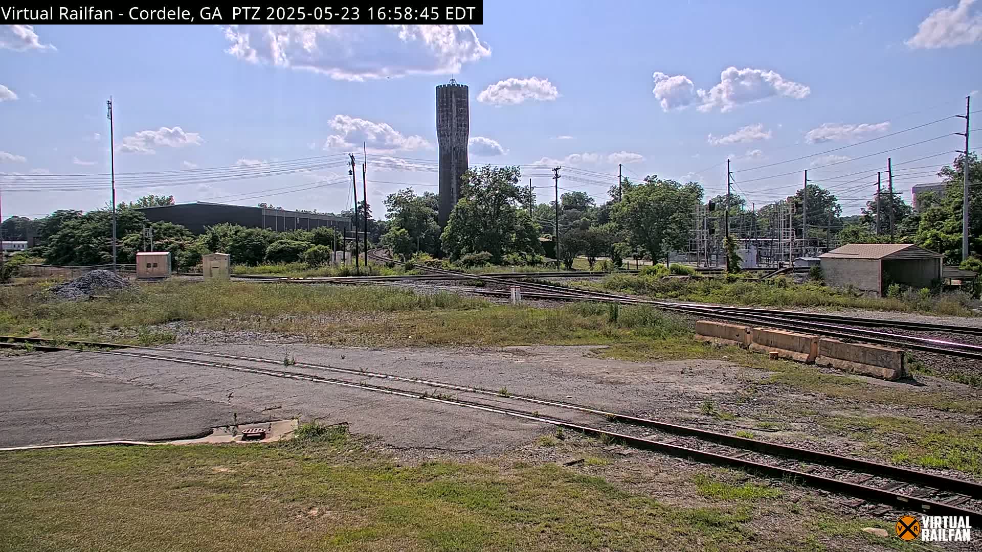 A tall, slender water tower is visible in the distance beyond a railway switching yard under a partly cloudy sky.