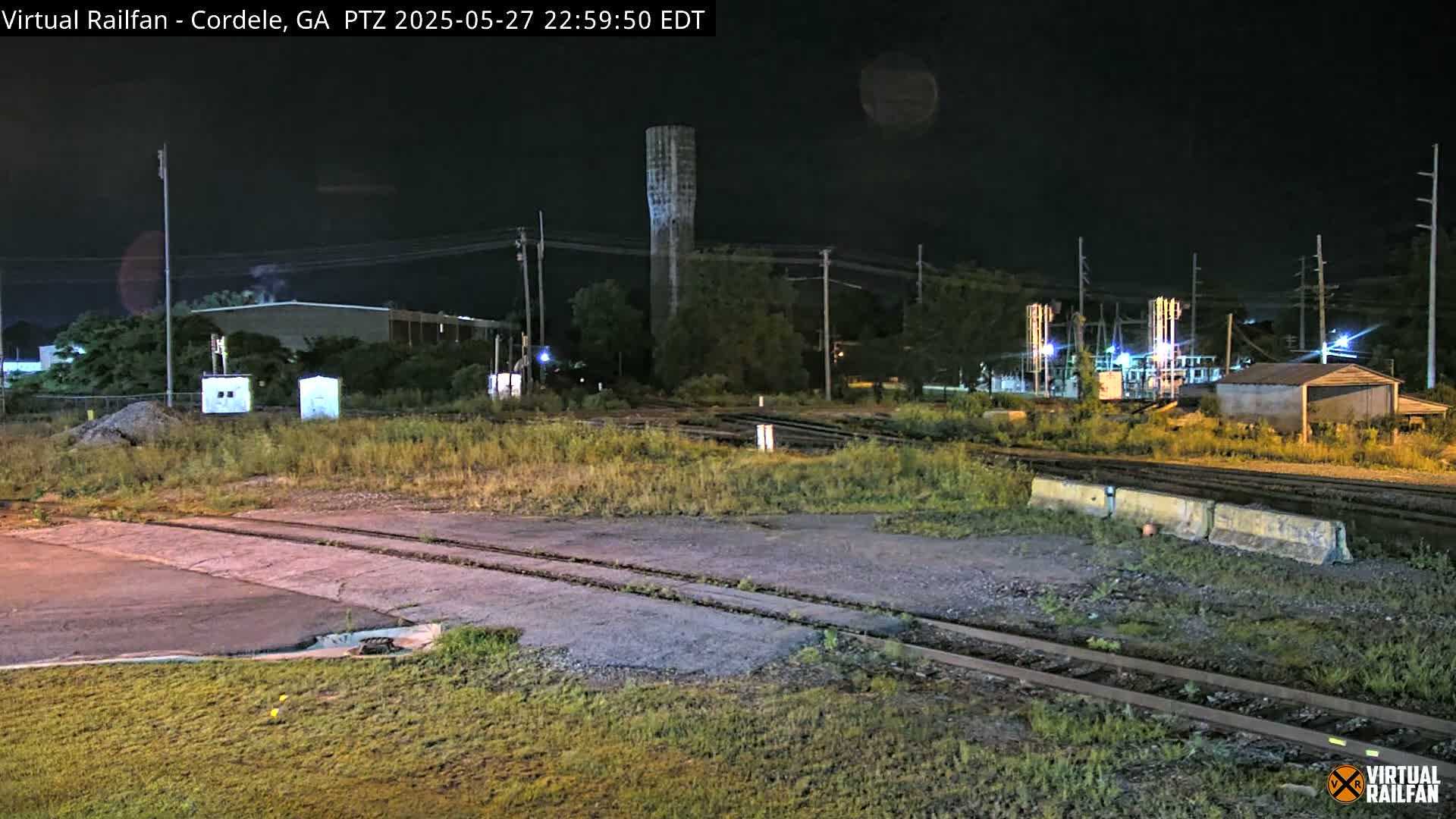 A nighttime view of a railroad crossing with a water tower in the background under a clear, dark sky.