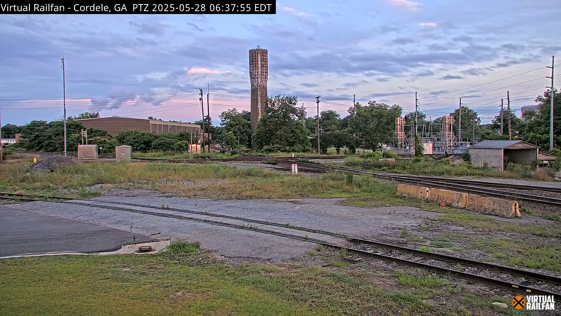 A rail yard with a tall water tower in the background under a partly cloudy evening sky.