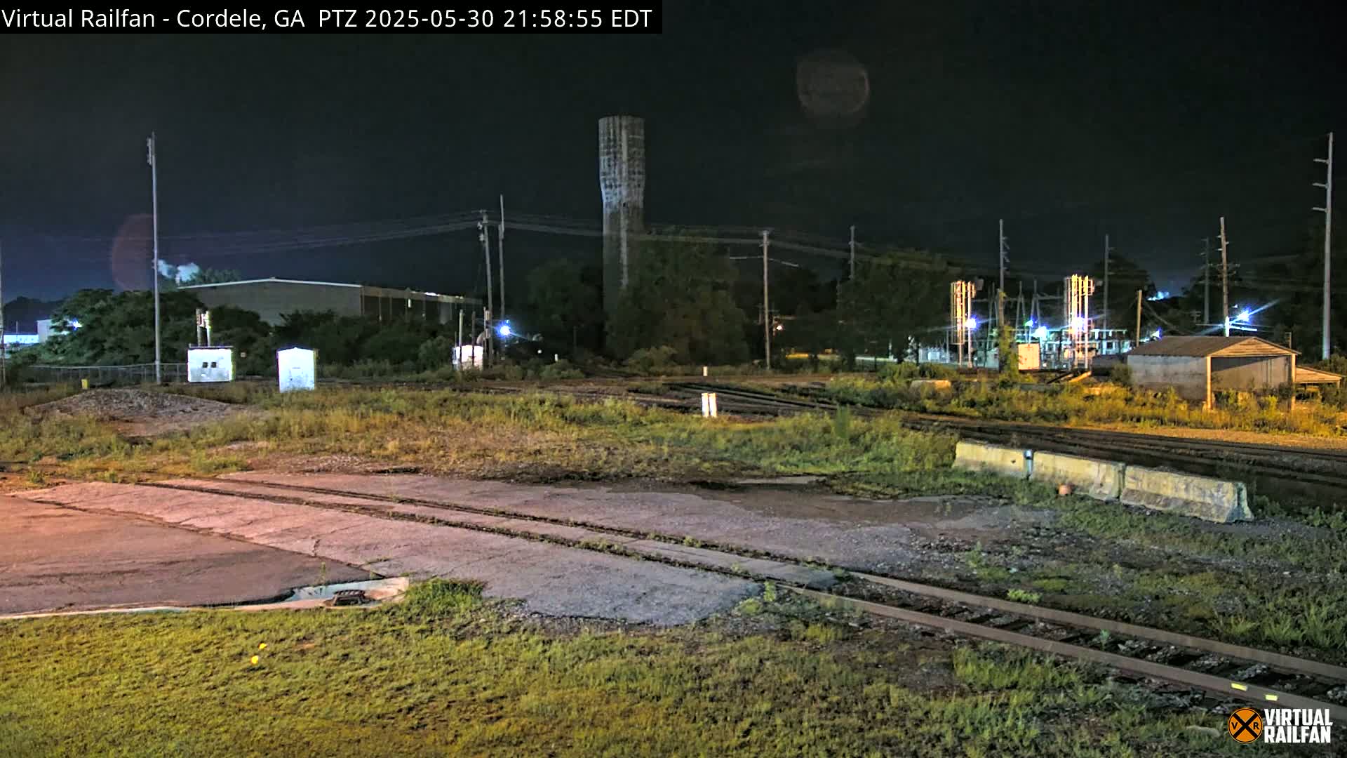 A nighttime view of railroad tracks and industrial buildings under a dark sky.