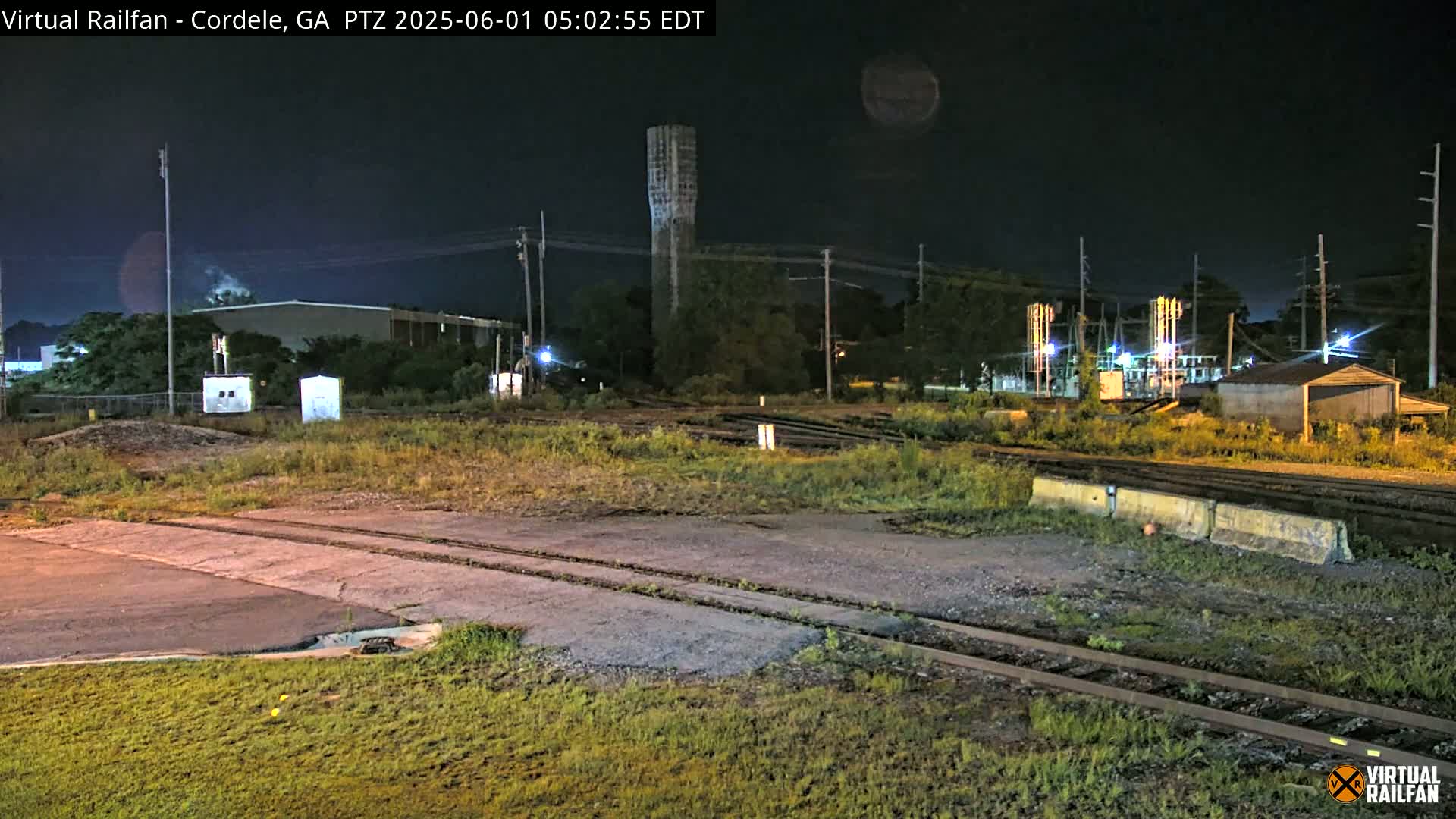 A nighttime view of railroad tracks and industrial buildings under a clear, dark sky.