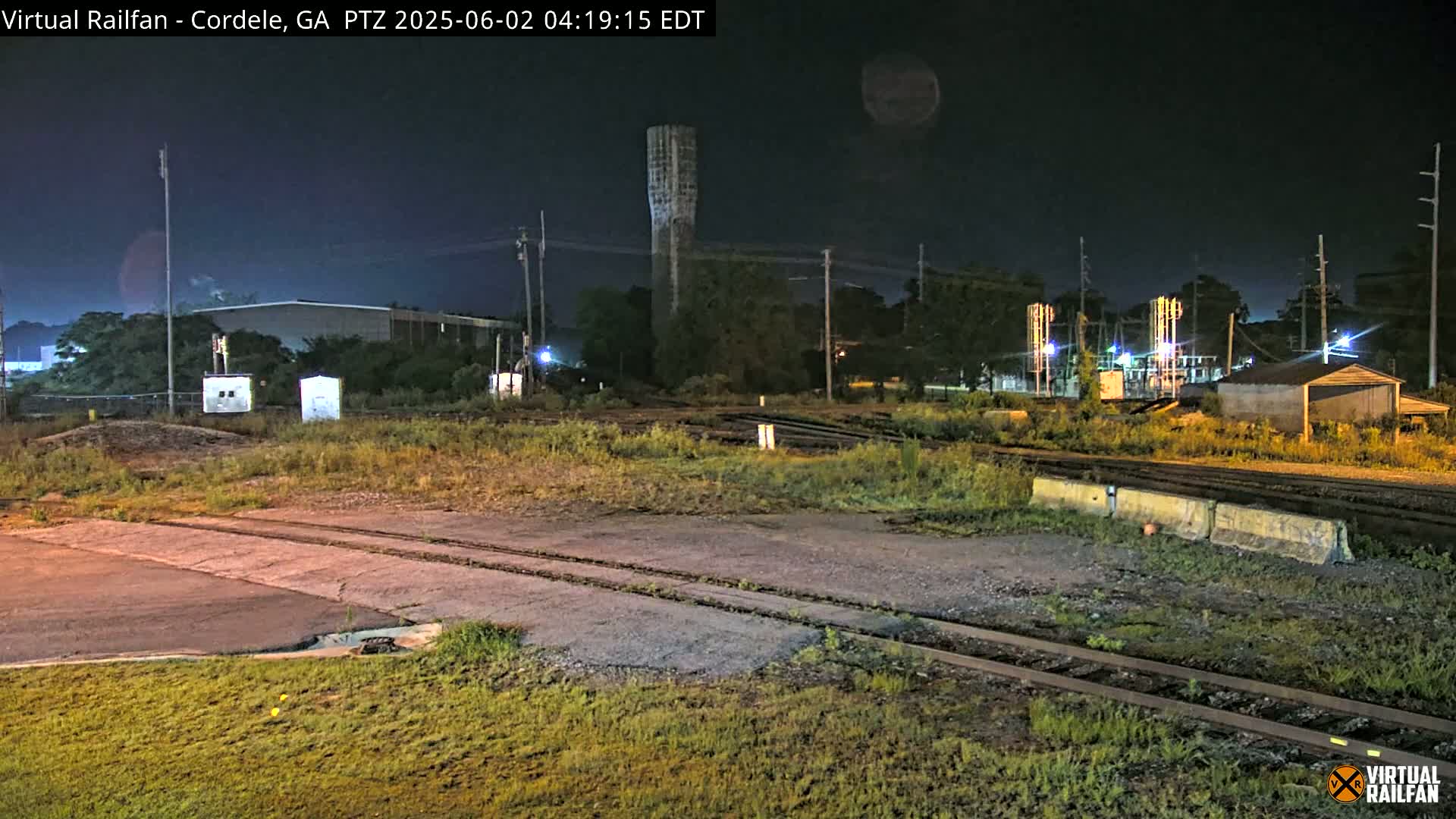 A nighttime view of railroad tracks and industrial buildings under a dark sky.