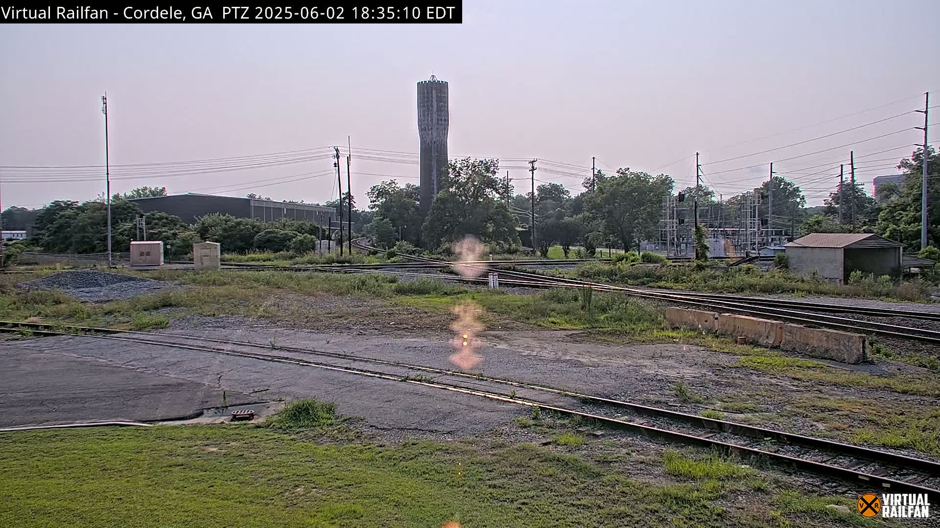 A railroad switching yard with a tall water tower in the background on a partly cloudy day.