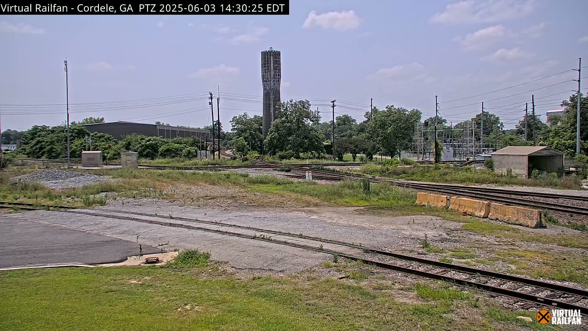 A train yard with a water tower in the background on a partly cloudy day.