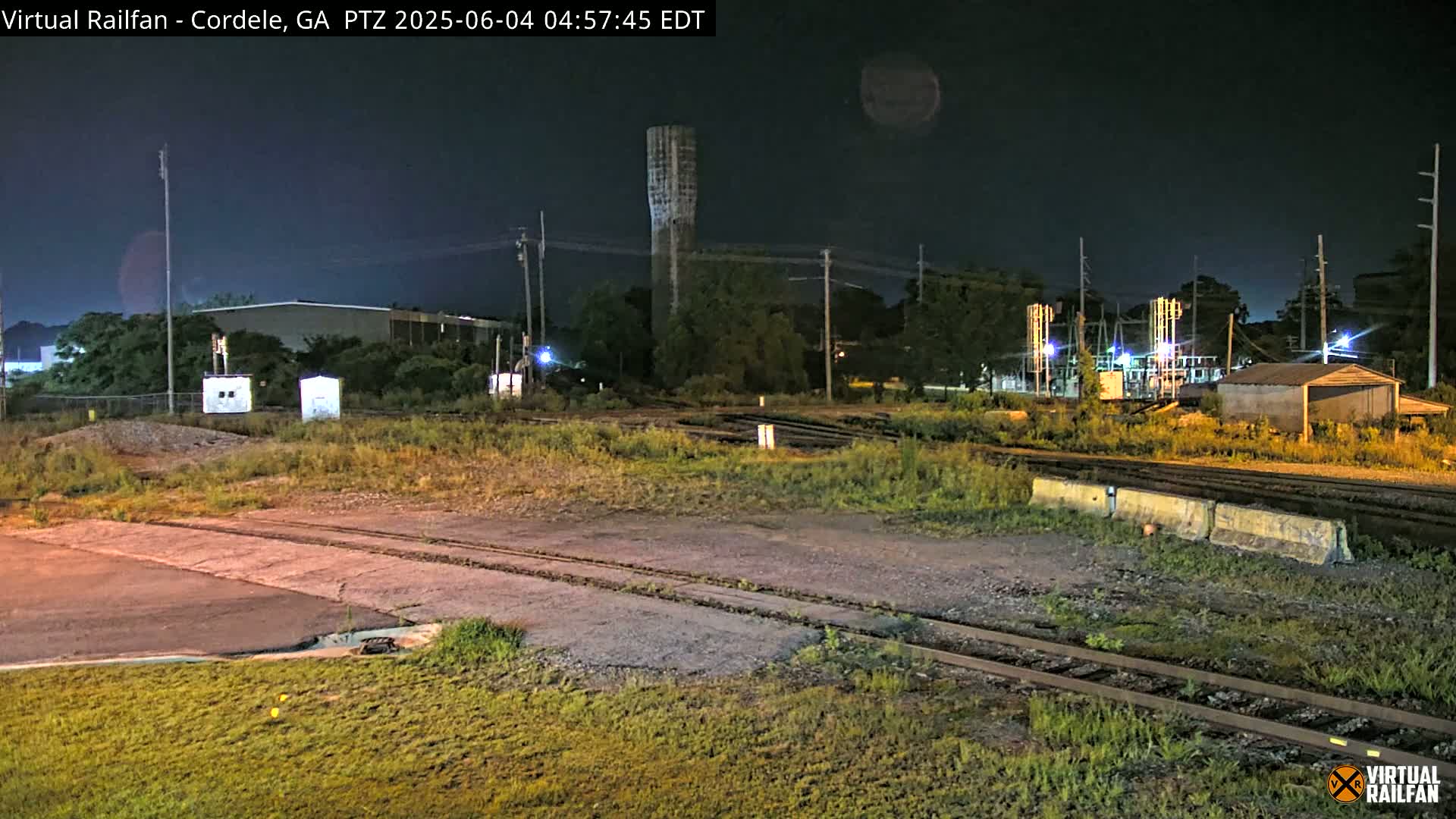 A nighttime view of a railroad crossing with a water tower in the background, under a clear, dark sky.