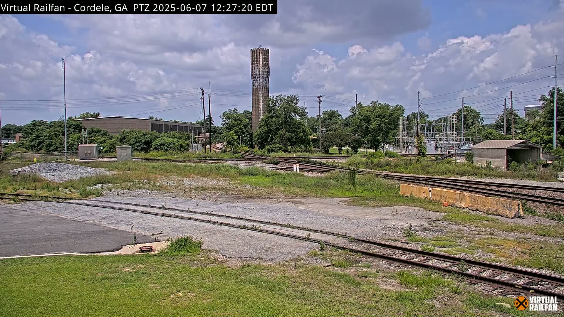 A railway switching yard with a water tower in the background under a partly cloudy sky.