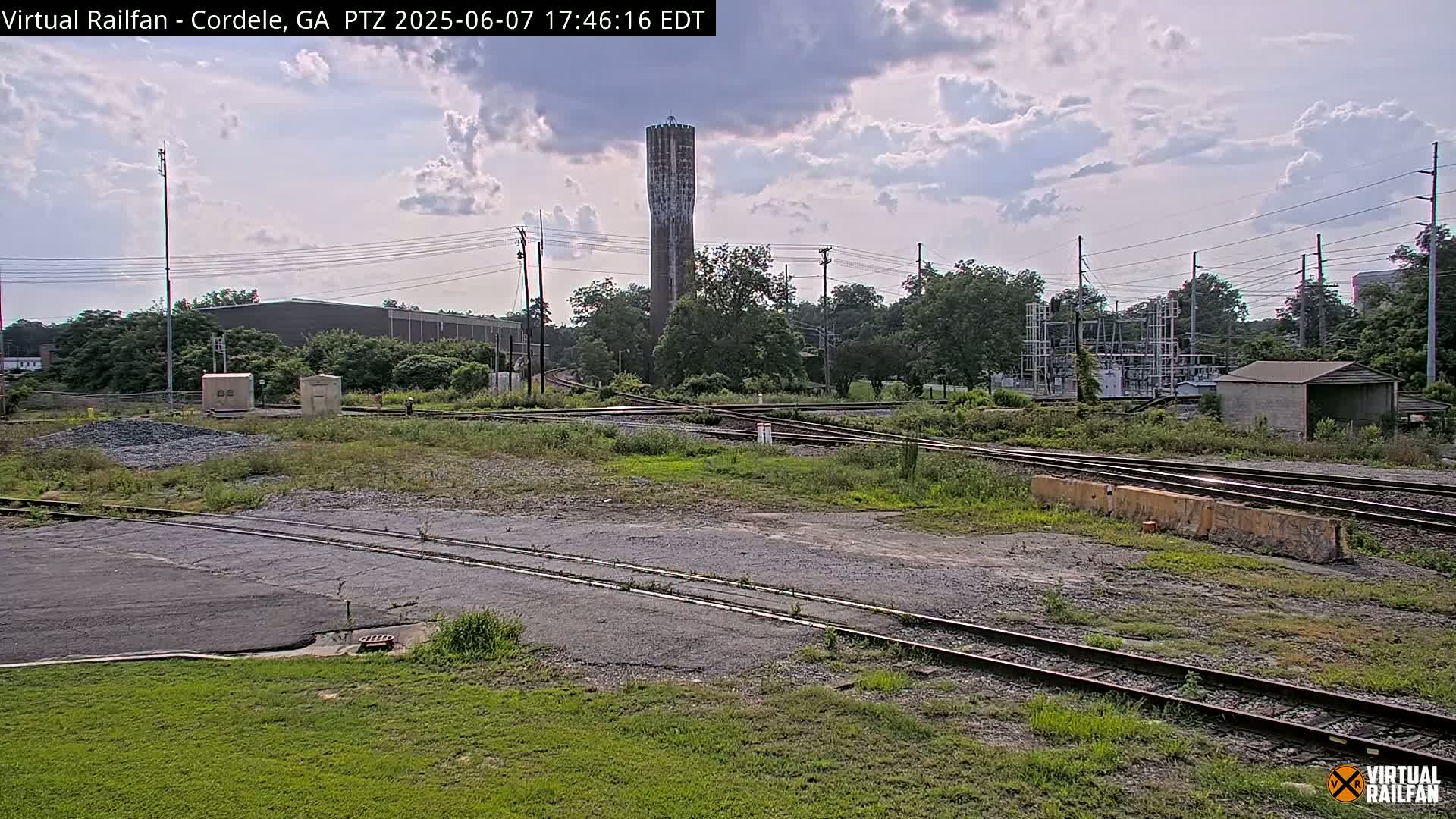 A partly cloudy sky overlooks a railroad yard with a tall water tower in the background.
