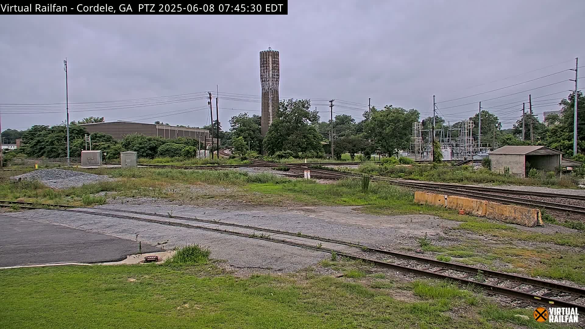A view of a railway switching yard under a cloudy sky, featuring a tall water tower in the background.