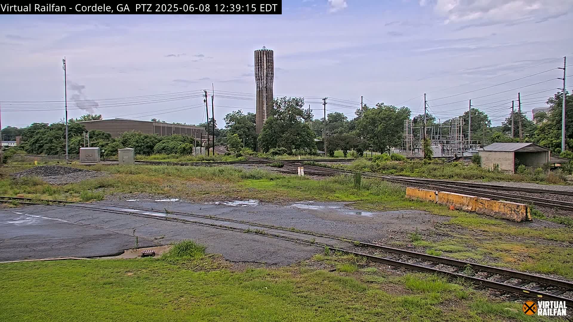 A view of a railway switching yard with a tall water tower in the background on an overcast day.