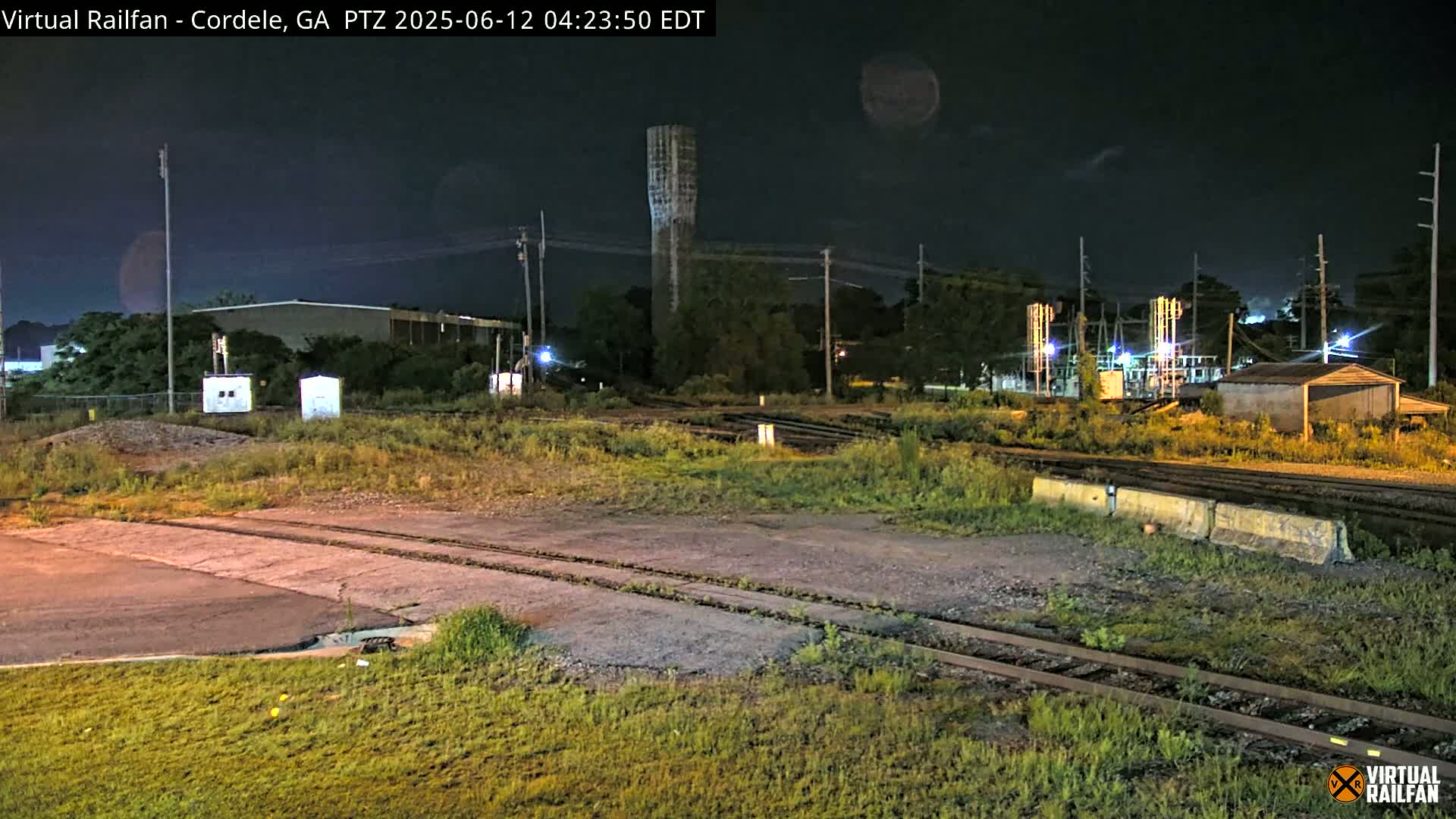 A nighttime view of railroad tracks and industrial buildings under a dark, clear sky.