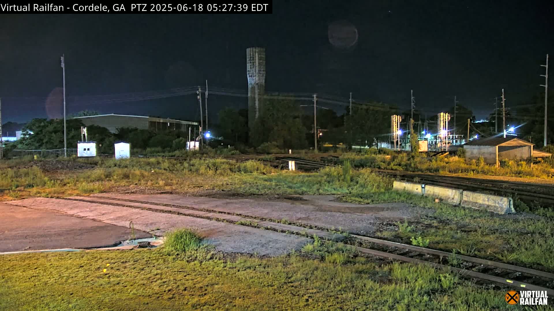 A nighttime view of railroad tracks and industrial buildings under a clear, dark sky.