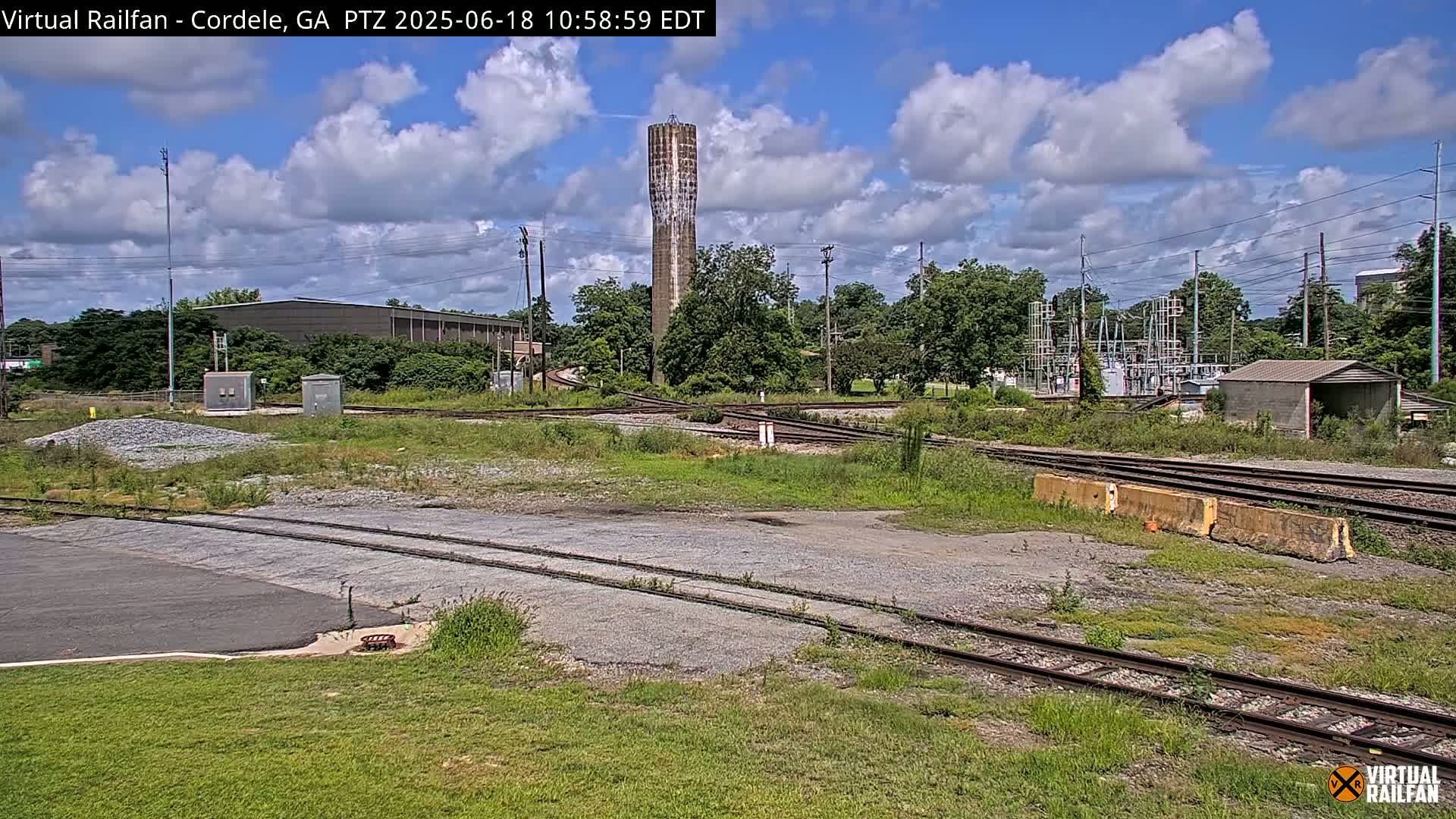A railroad switching yard with a tall water tower in the background under a partly cloudy sky.